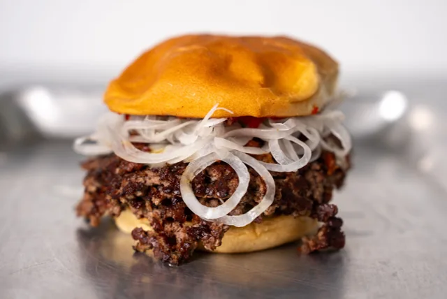A beef burger topped with fresh onion and melted cheese