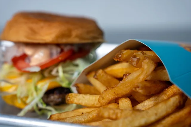 Golden hand-cut fries in a blue sleeve, with a burger in the background
