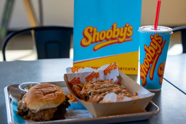 A burger and loaded fries with a Shooby’s cup and branded bag