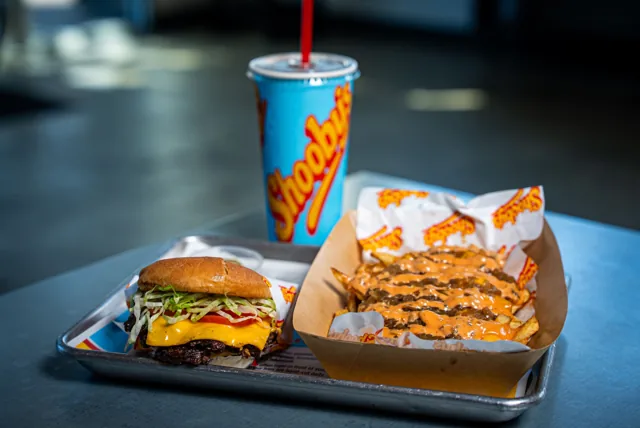 A cheeseburger and loaded fries with a blue Shooby’s cup