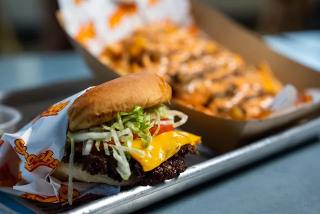 A close-up cheeseburger with loaded fries behind it