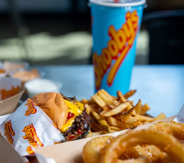 A meal with crisp onion rings in the foreground, a burger and fries