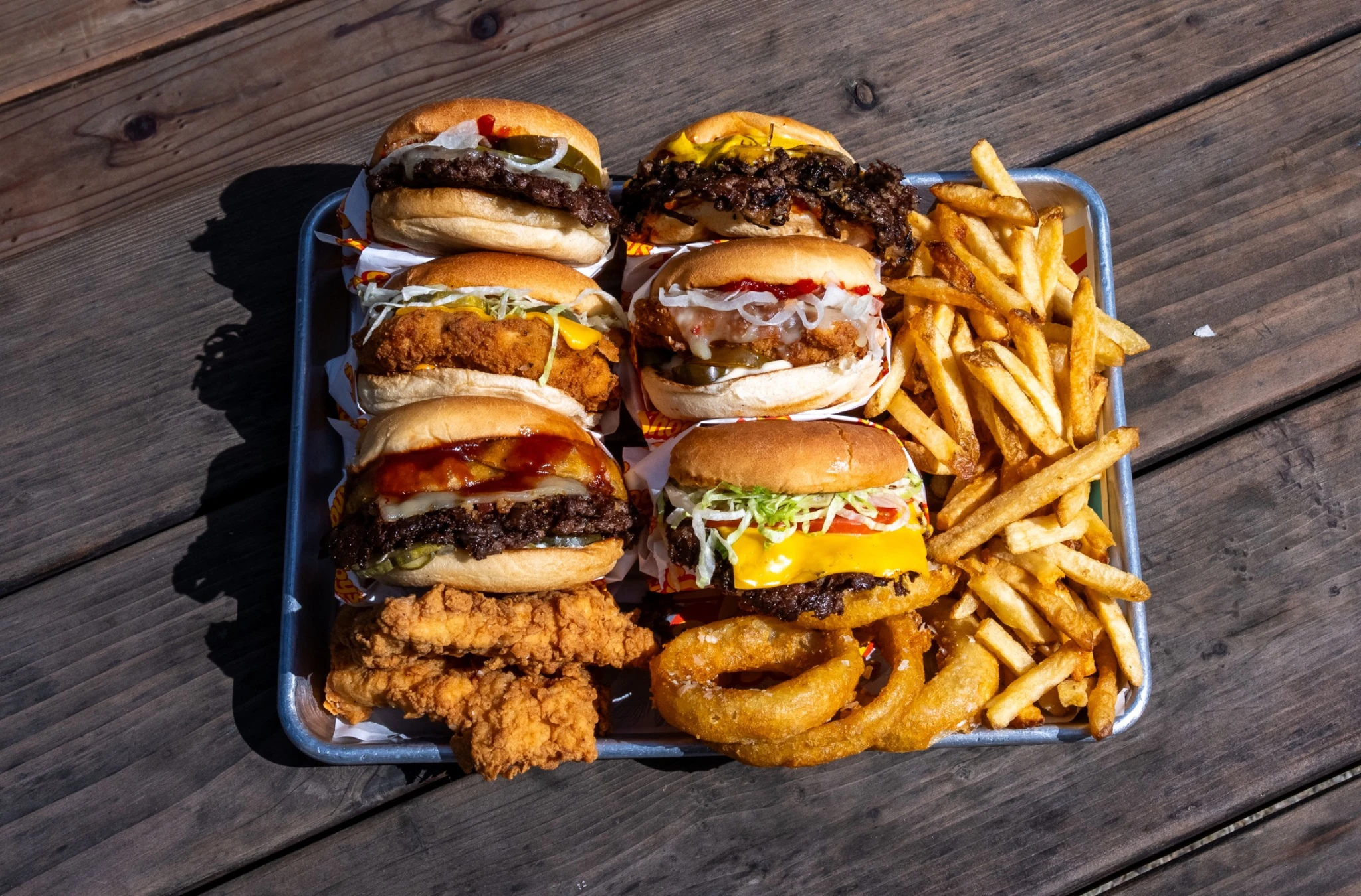 An overhead spread of Shooby’s burgers with visible beef patties, chicken sandwiches, hand-cut fries and onion rings