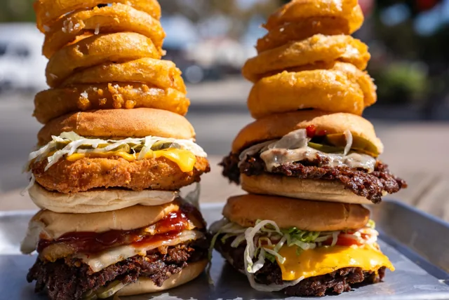 Two burger stacks topped with golden onion rings