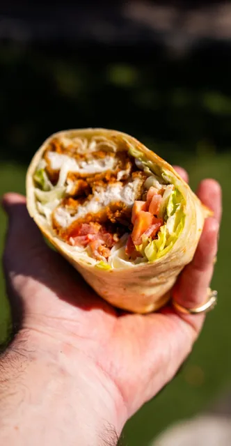 A freshly cut chicken wrap held up against a dark background