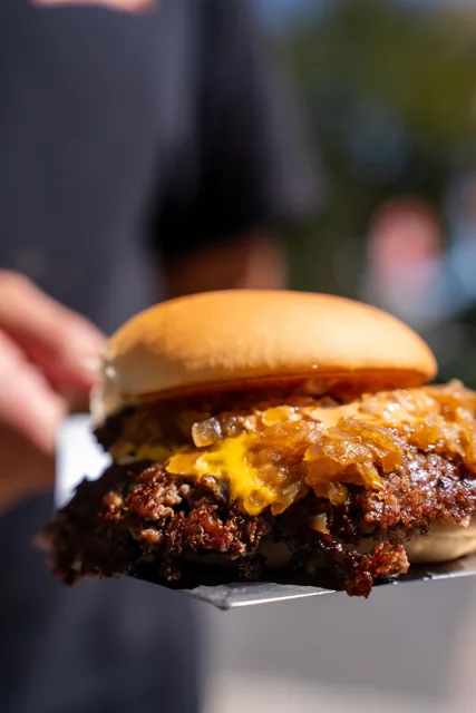 A cheeseburger with caramelized onions held on a spatula