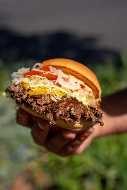 A classic burger with lettuce and tomato held outside