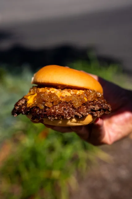 A hand-held cheeseburger with the beef patty in focus